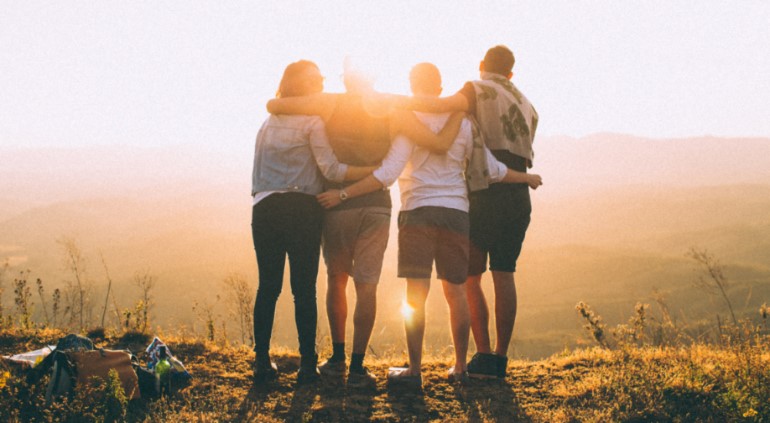 Four people hug in sunlight